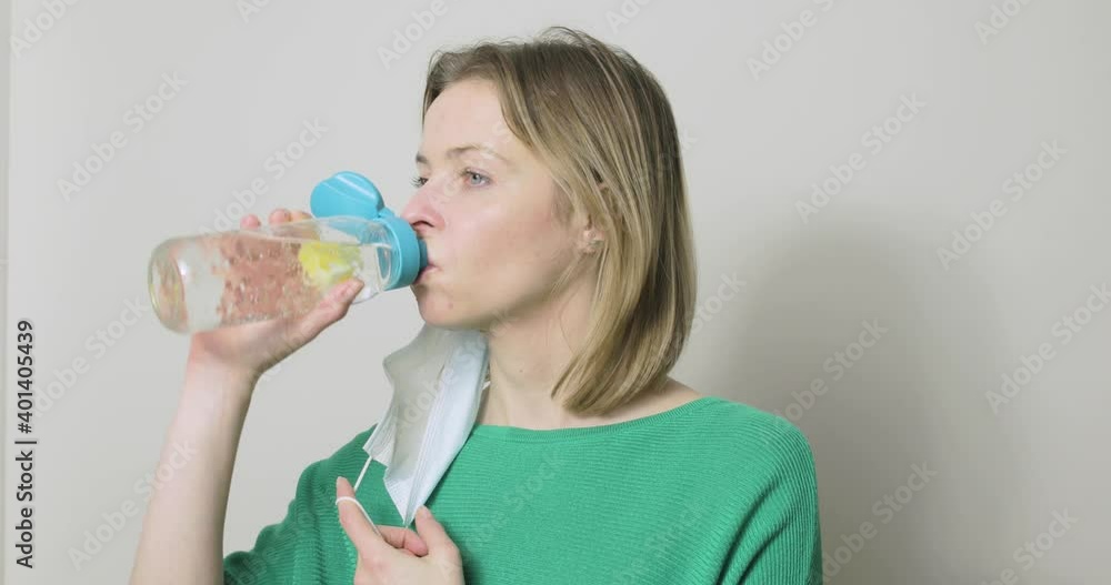 A woman has to remove her PPE mask before she can drink from her water bottle. A woman has to remove her PPE mask before she can drink from her water bottle.