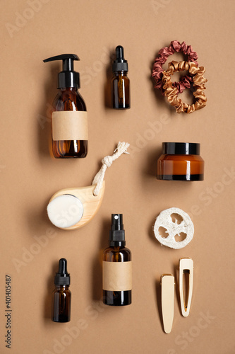 Set of amber glass bottles with blank labels and female bathroom accessories on brown background. SPA cosmetics set. Flat lay, top view