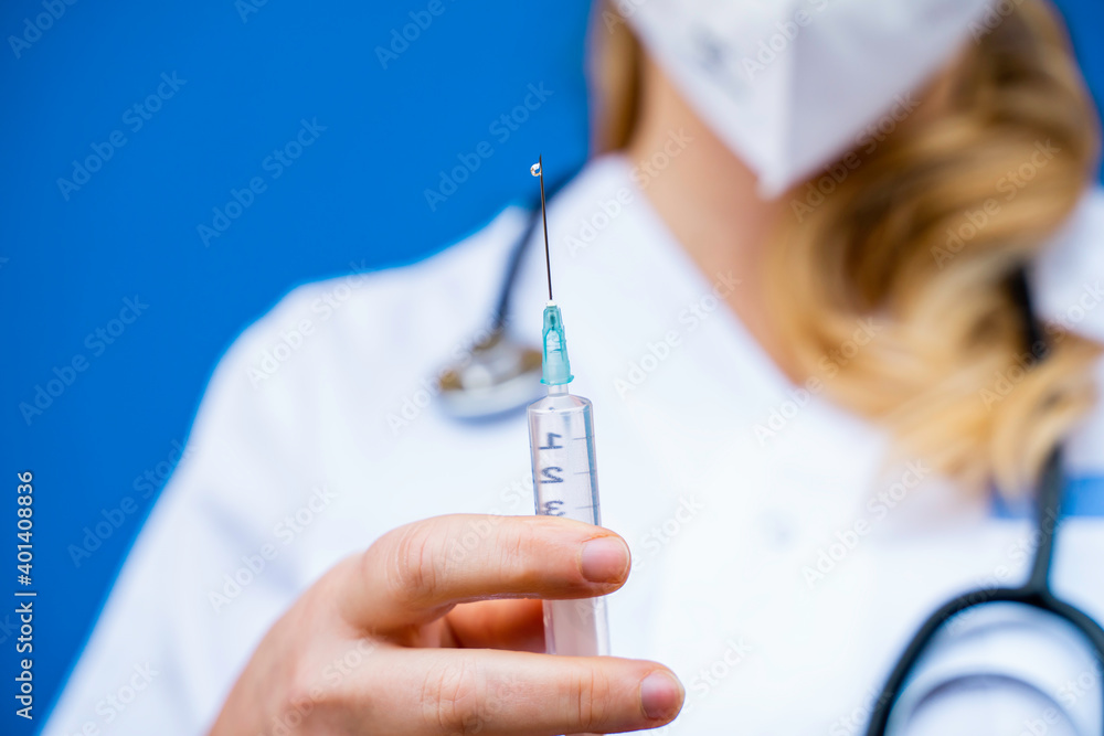 Nurse in front of a blue background holding a syringe and preparing the therapy to be injected to patients. Nurse in front of a blue background holding a syringe and preparing the therapy to be injected to patients.