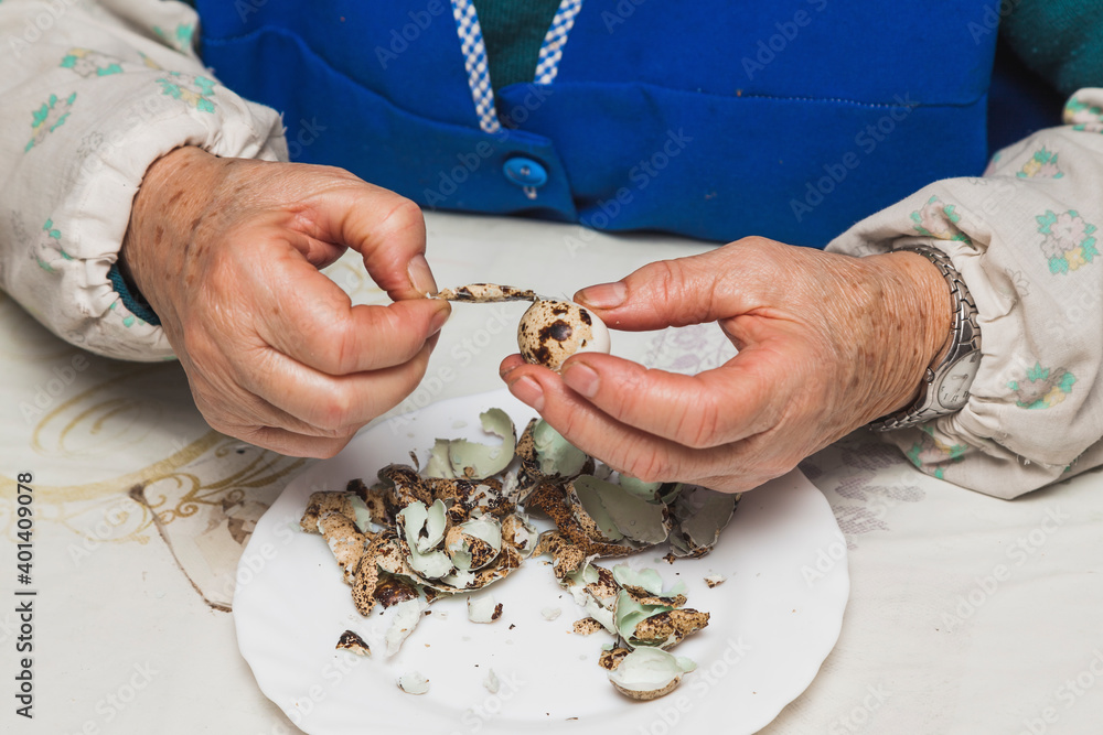 The hands of an elderly lady peeling a quail egg