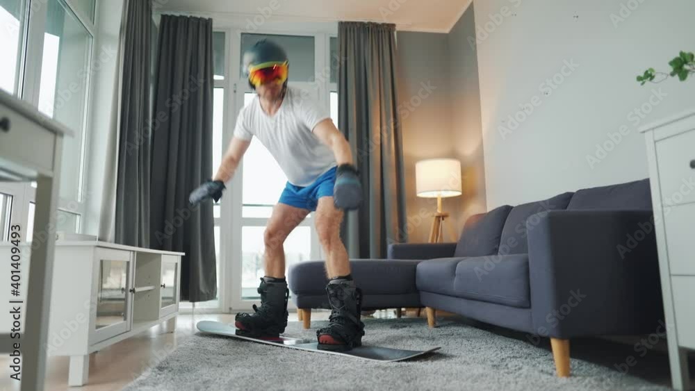 Fun video. Man in shorts and a T-shirt depicts snowboarding on a carpet in a cozy room. Waiting for a snowy winter Fun video. Man in shorts and a T-shirt depicts snowboarding on a carpet in a cozy room. Waiting for a snowy winter