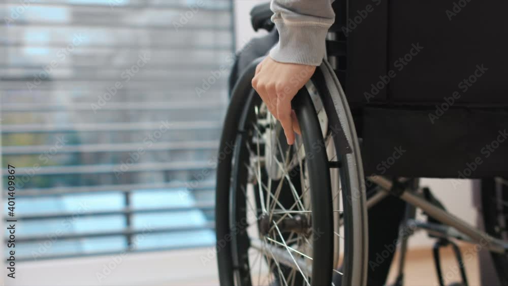 Close up of man on wheelchair pushing with hands in a living room and looking through window. Close up of man on wheelchair pushing with hands in a living room and looking through window.