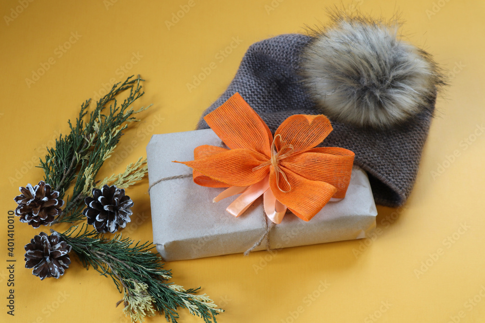 Fototapeta premium Christmas gift with yellow bows in winter gray hat on yellow background, top view, place for text