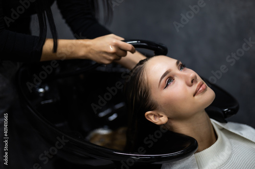 Smiling attractive woman with her eyes closed in enjoyment having a hair shampoo at the hair salon