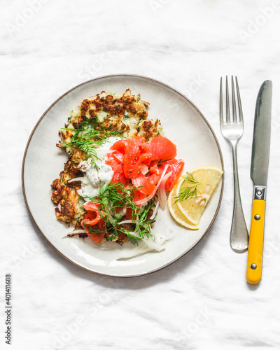 Cauliflower fritters with smoked salmon and greek yogurt sauce on a light background, top view
