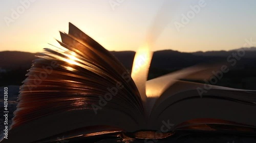 Inspiration and wisdom concept. Open book with pages moving in the wind at sunset or sunrise sunlight, warm light.