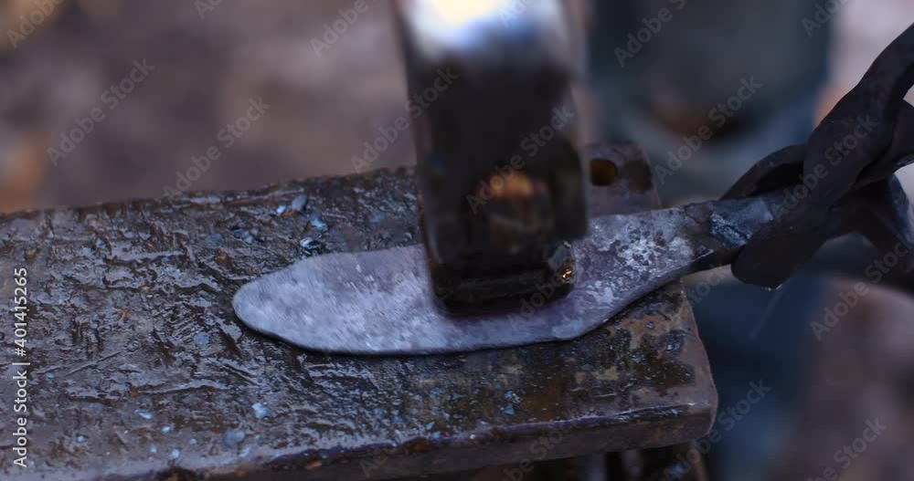 Selective focus of hands of young female craftsman, hitting hammer on a chisel making a knife while doing process of forging on anvil in workshop Selective focus of hands of young female craftsman, hitting hammer on a chisel making a knife while doing process of forging on anvil in workshop