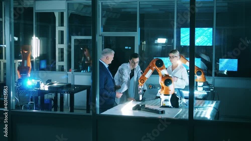 Three engineers discussing industrial robot capabilities at laboratory. Team of industrial robotics engineers working with robot arm. photo