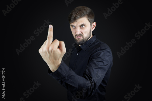 a man in a black shirt and on a black background shows his middle fingers makes obscene gestures