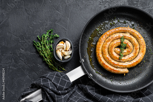 Grilled spiral sausages with garlic and seasoning in a pan. Black background. Top view. Copy space