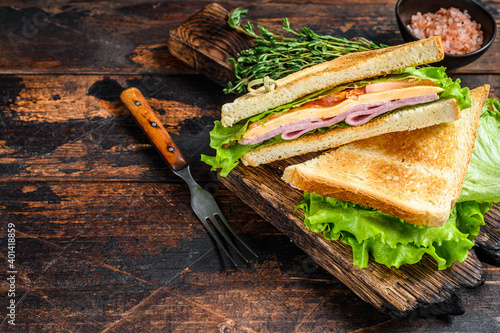 Turkey Ham Club sandwiches with cheese, tomatoes and lettuce on a wooden cutting board. Dark wooden background. Top view. Copy space