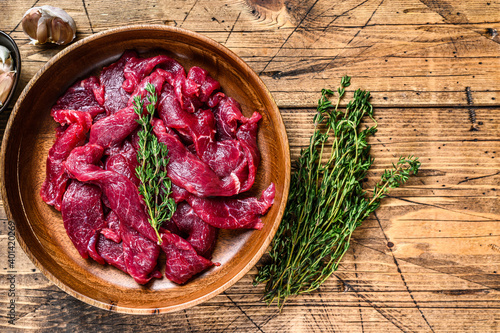 Raw uncooked beef meat sliced in strips with fresh herbs for beef stroganoff. wooden background. Top view. Copy space