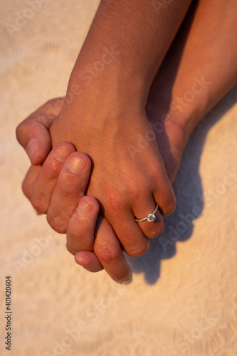 Couple clasping hands showing engagement ring in the sunset