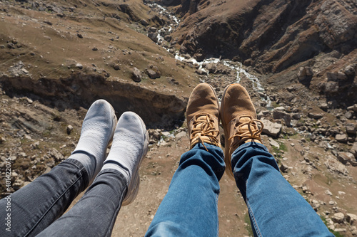 Legs of a man and a woman over a cliff and a mountain river.