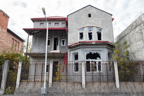 Fotografia abandoned two-story house with broken windows behind a high lattice fence