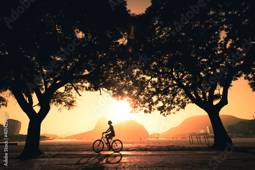 Silhouette of a Woman Cycling Under Trees in the Early Morning during Beautiful Warm Sunrise in Rio de Janeiro with Sugarloaf Mountain in the Horizon photo