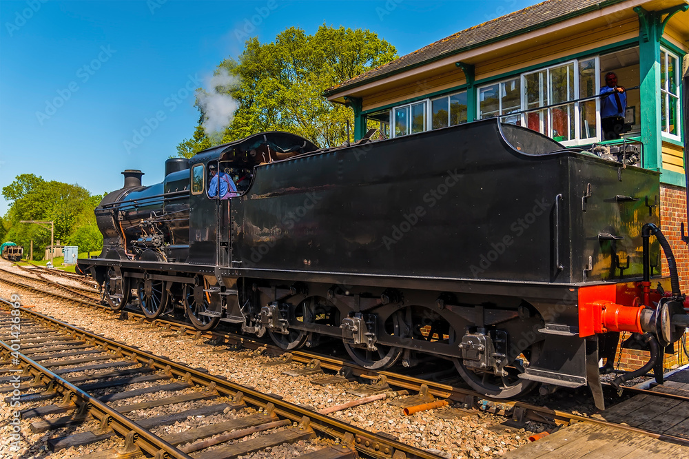 A steam train passing a signal box on a railway line in the UK on a sunny summer day