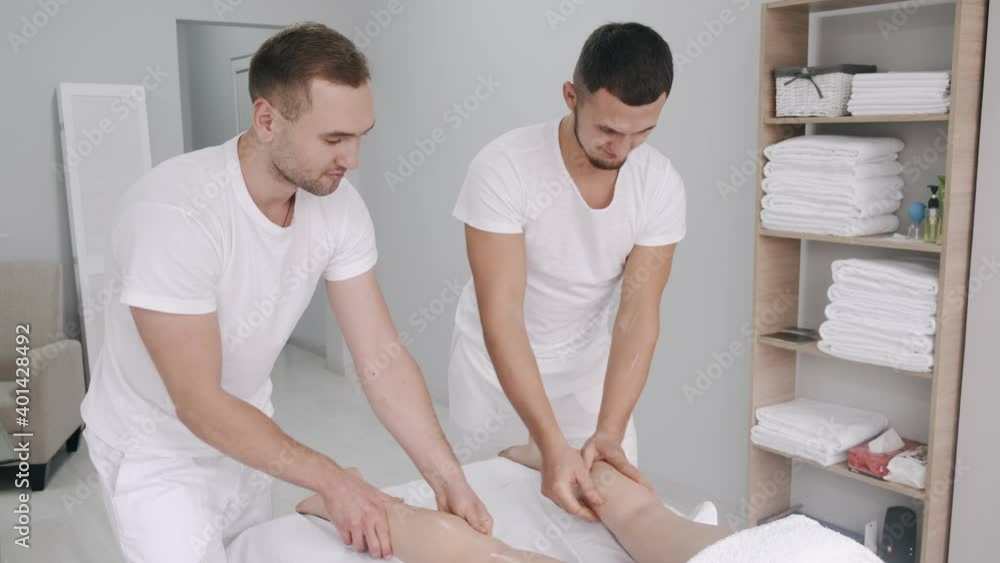 At the same time by two masseurs knead calf muscles and feet of girl lying on the couch. Health care and wellness. Therapeutic foot massage. At the same time by two masseurs knead calf muscles and feet of girl lying on the couch. Health care and wellness. Therapeutic foot massage.