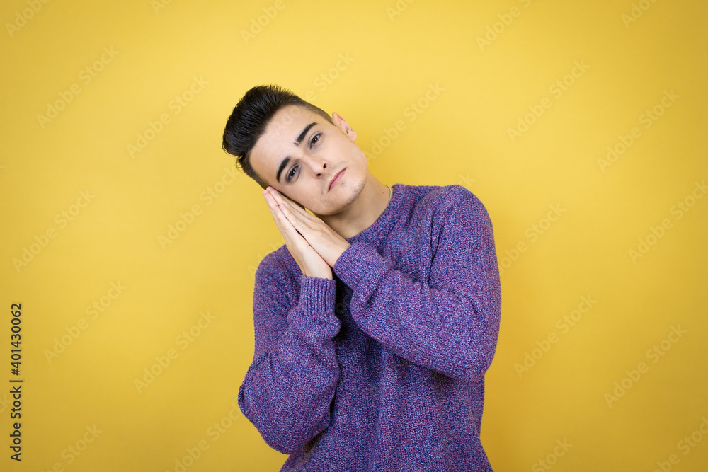 Young caucasian man over isolated yellow background sleeping tired dreaming and posing with hands together while smiling with closed eyes. Young caucasian man over isolated yellow background sleeping tired dreaming and posing with hands together while smiling with closed eyes.