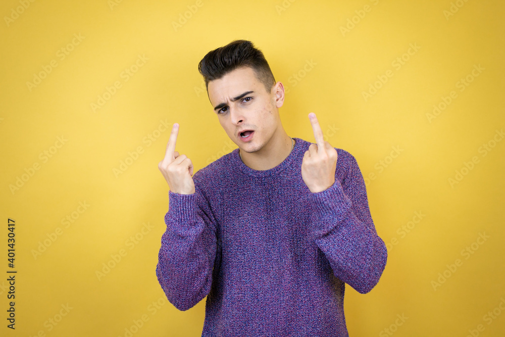 Young caucasian man over isolated yellow background showing middle finger doing fuck you bad expression, provocation and rude attitude. screaming excited Young caucasian man over isolated yellow background showing middle finger doing fuck you bad expression, provocation and rude attitude. screaming excited