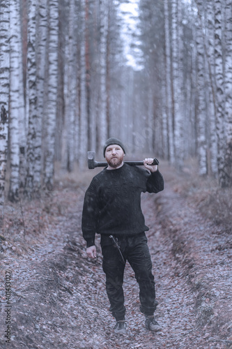 Portrait of a a bearded man with an axe at the late autumn or winter birch forest. Unfriendly stranger - a woodcutter (lumberjack), hermit, villager...