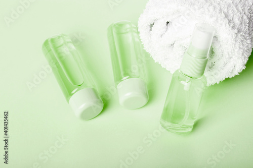 Three bottles of tonic or lotion and white towel on green background. Freshness and body care. Travel set of face care cosmetic. Three bottles of hand sanitizer. Liquid soap and sanitizer for hands