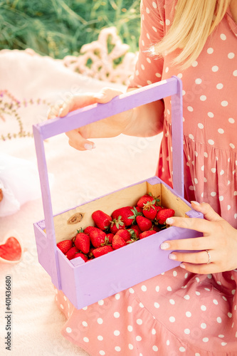 girl on a picnic in a spring park. female hands hold a purple wooden basket with strawberries.