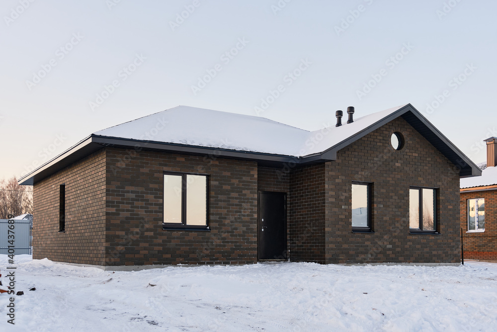One-story brick house on the background of a snowy winter evening. Construction of low-rise buildings for further sale. Concept of building business. One-story brick house on the background of a snowy winter evening. Construction of low-rise buildings for further sale. Concept of building business.