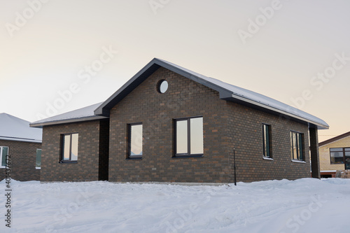 One-story brick house on the background of a snowy winter evening. Construction of low-rise buildings for further sale. Concept of building business. © Мaksim G