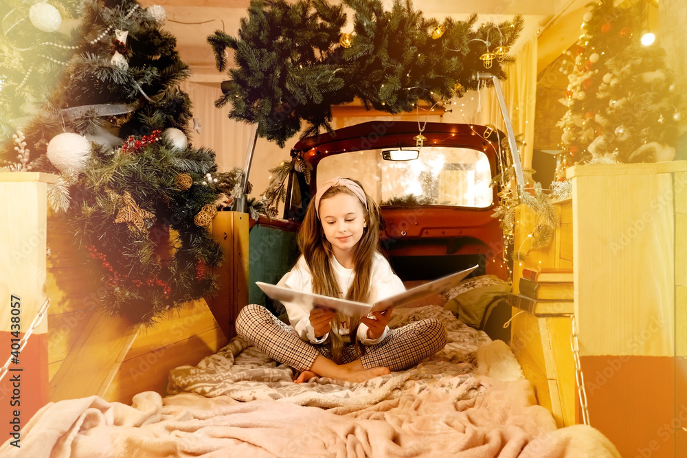 cute beautiful long-haired girl writing a letter to santa claus. New Year's atmosphere, make a wish. the child sits in the car and reads a book..