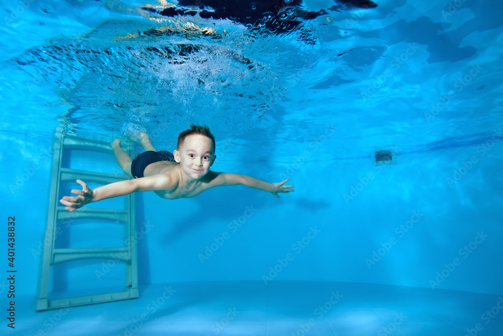 Beautiful athletic boy swims underwater in the pool. Merrily dives under the water from the stairs. Swimming classes. Bodily exercises. Healthy lifestyle