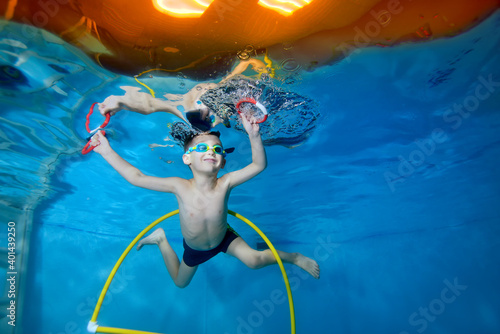 Portrait of a little boy in class underwater in a children's pool. He swims through the Hoop, pulls out toys. Active happy child. Healthy lifestyle. Swimming lessons under the water. A family sport photo