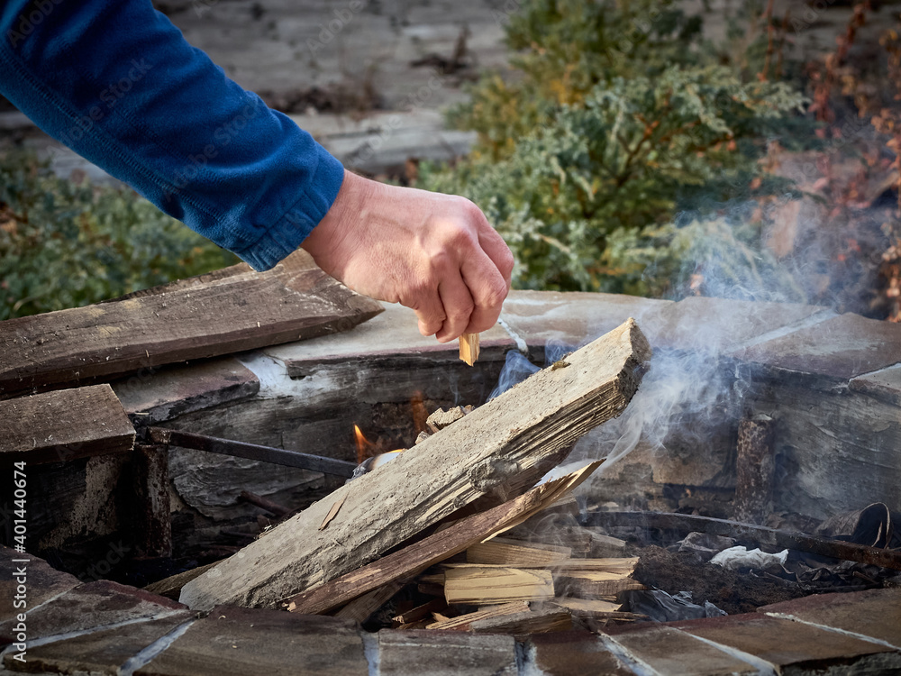 Man touching wooden log while making bonfire near stones Man touching wooden log while making bonfire near stones