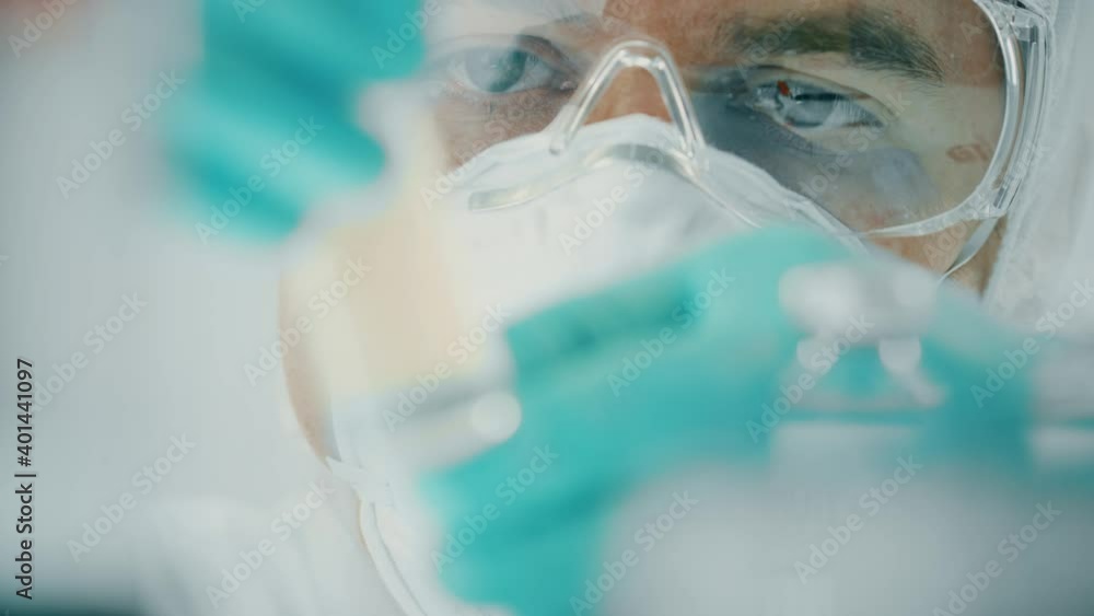 Researcher wearing protective gear checks a vial with COVID-19 vaccine in his hands, close-up shot Researcher wearing protective gear checks a vial with COVID-19 vaccine in his hands, close-up shot