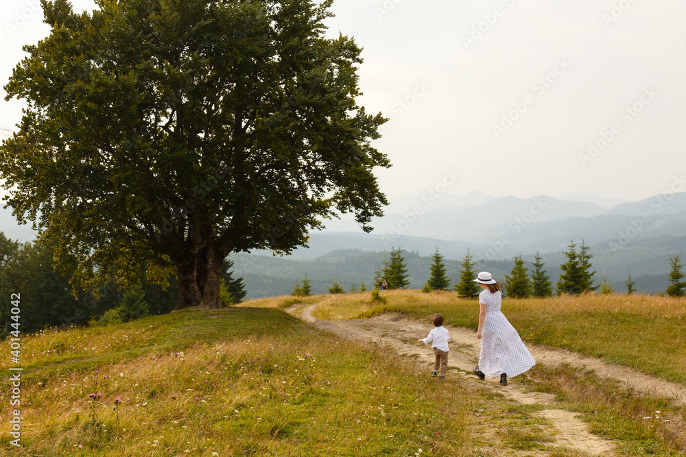 Romantic woman weared in dress, hat and son on background of Carpathian landscape. Vintage portrait. Dirt road in the mountains. Carpatians, Ukraine. Coniferous forest and beautiful sky. Beech tree Romantic woman weared in dress, hat and son on background of Carpathian landscape. Vintage portrait. Dirt road in the mountains. Carpatians, Ukraine. Coniferous forest and beautiful sky. Beech tree