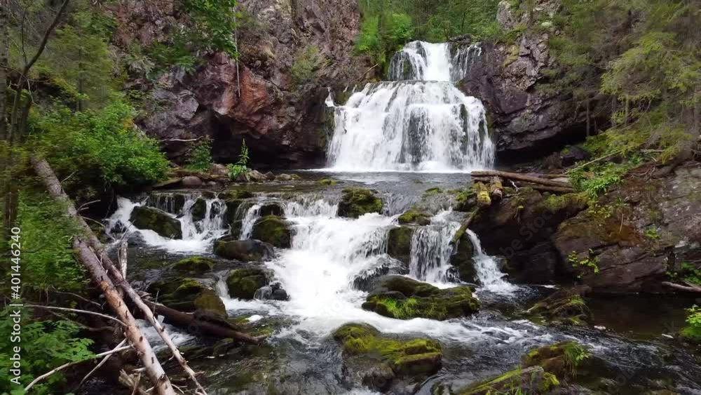 A beautiful waterfall in a forest. The camera on the drone gradually moves away from the falling water. A beautiful waterfall in a forest. The camera on the drone gradually moves away from the falling water.