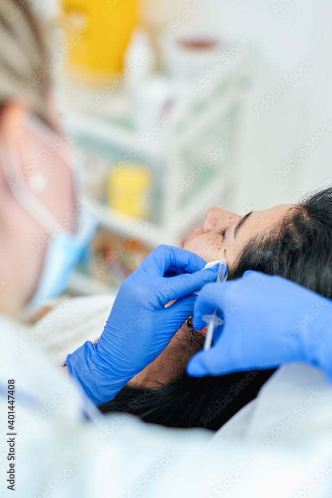 Close up of hands of cosmetologist making botox injection. She is holding syringe. Woman is receiving procedure with enjoyment. High quality photo