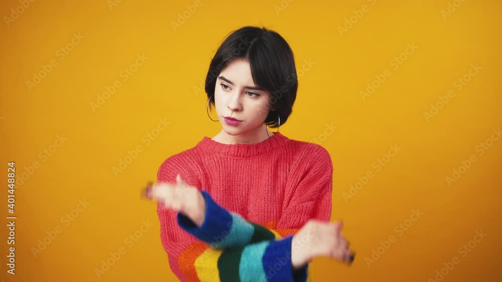 Serious young woman in red sweater with rainbow sleeves crossing hands, gesturing stop , orange background Serious young woman in red sweater with rainbow sleeves crossing hands, gesturing stop , orange background