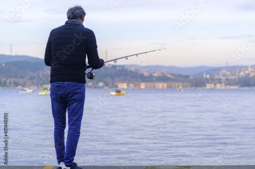 Man is fishing at the Bosphorus, alone and lonely man waiting fishes to catch with copy space and space for text, small boats are fishing on the sea. Depression concept