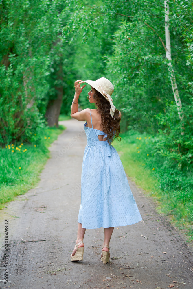 beautiful girl in a straw hat and blue dress on the road in the Park
