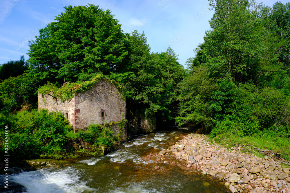 Old ruin of an abandoned mill by a small river and fall, being overtaken by vegetation