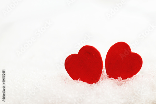 Two wooden red hearts on a white snowy background close-up. Copy space. Valentine s Day concept. Love