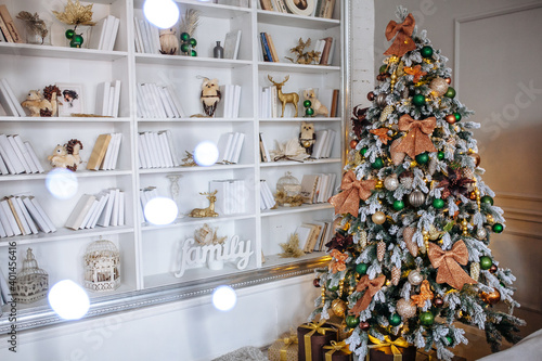 The bedroom decorated for Christmas. Cozy home interior. New year decoration. White room with large bookshelves.. Christmas tree with shyning garland