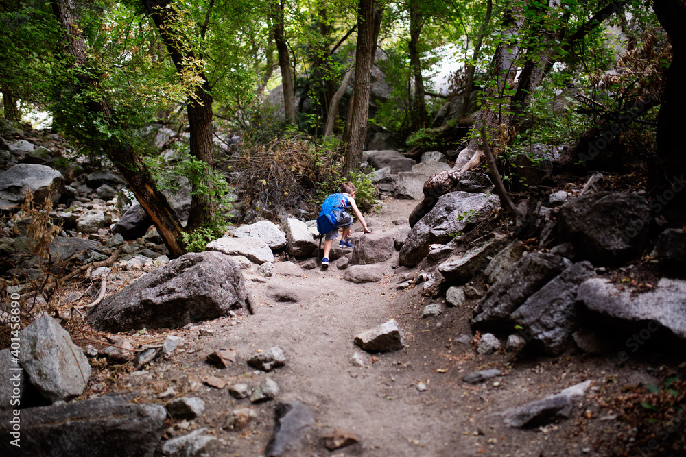 young boy with a backpack hiking up a rocky trail