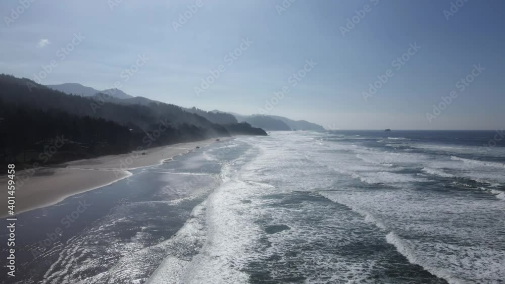 Descending over calm ocean waves breaking on a sun glistening beach, aerial Descending over calm ocean waves breaking on a sun glistening beach, aerial