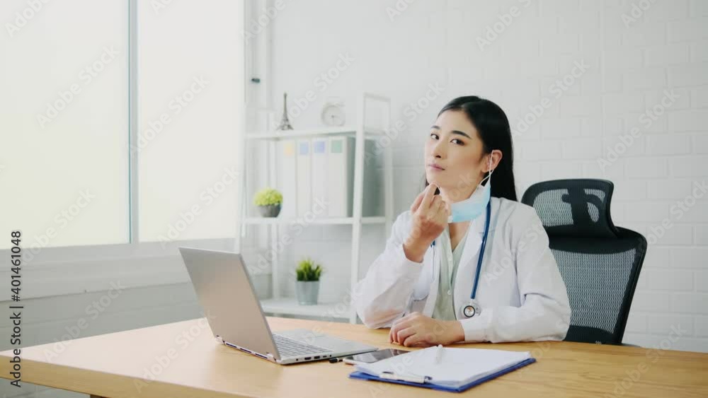 Happy doctor takes off mask. Copy space at right side on gray background. Smiling woman took off her mask rejoicing at good news about the end of pandemic. Coronavirus concept.
