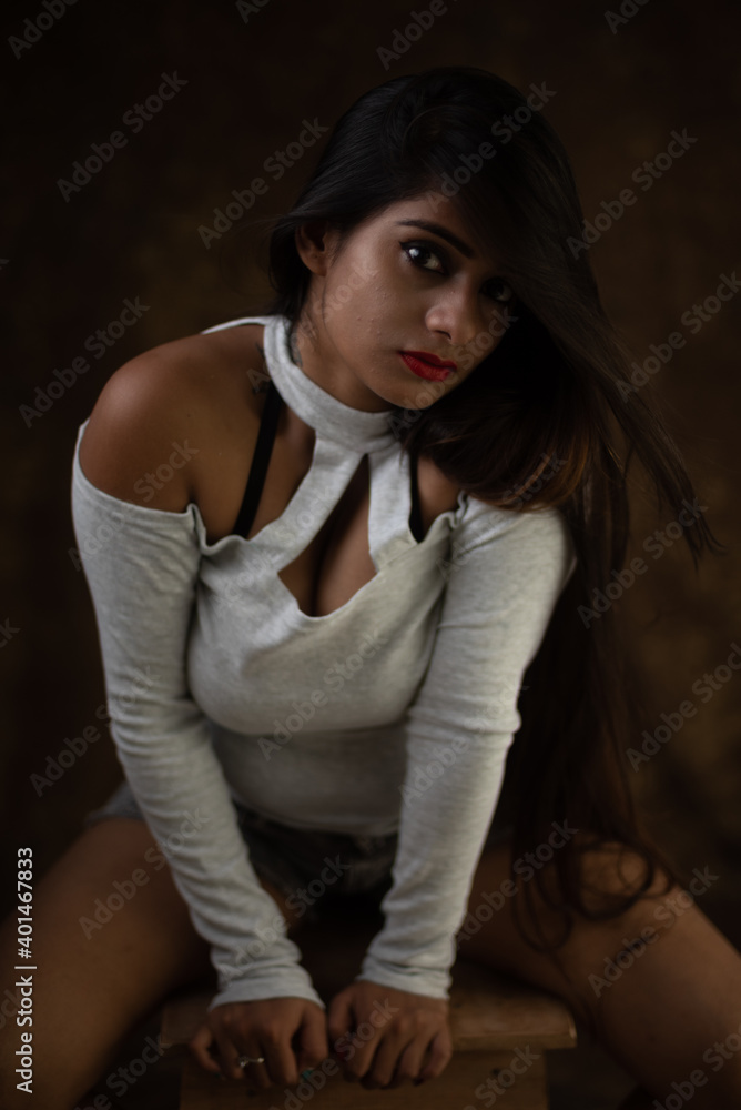 Fototapeta premium Studio portrait of a beautiful and young Indian Bengali female model in white cold shoulder top and jeans hot pant. Indian fashion and models