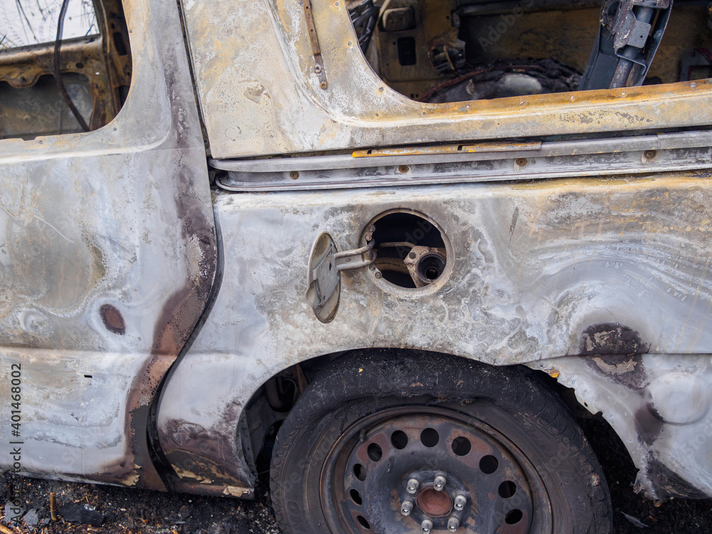 Closeup of passenger side of abandoned and burned car showing gas tank, melted tire and rear quarter panel