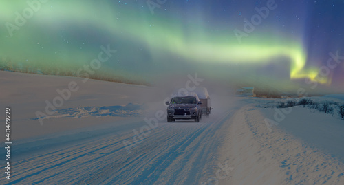 SUV rides on a winter forest road with Aurora - A car in a snow-covered road among trees and snow hills