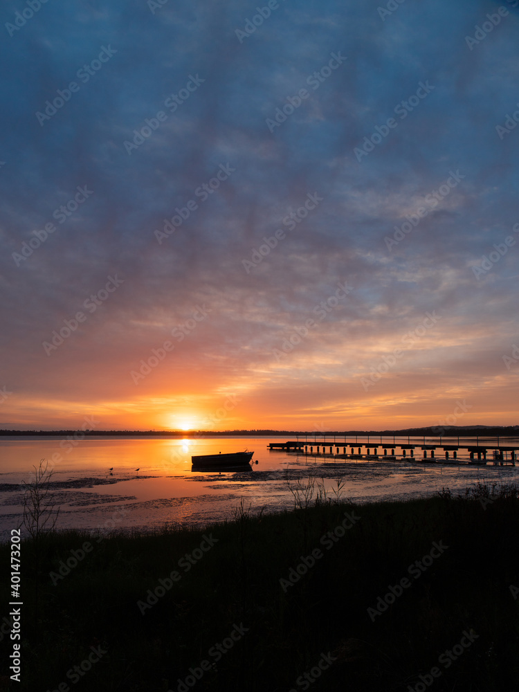 Boat and jetty silhouette on the lake side during sunrise.